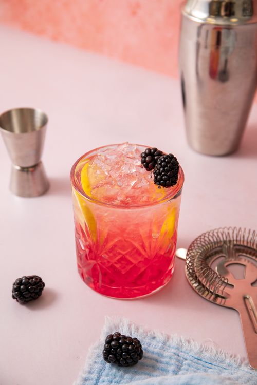 Free Delicious homemade blackberry cocktail with lemon slices in a crystal glass on a pink background, ideal for refreshment. Stock Photo