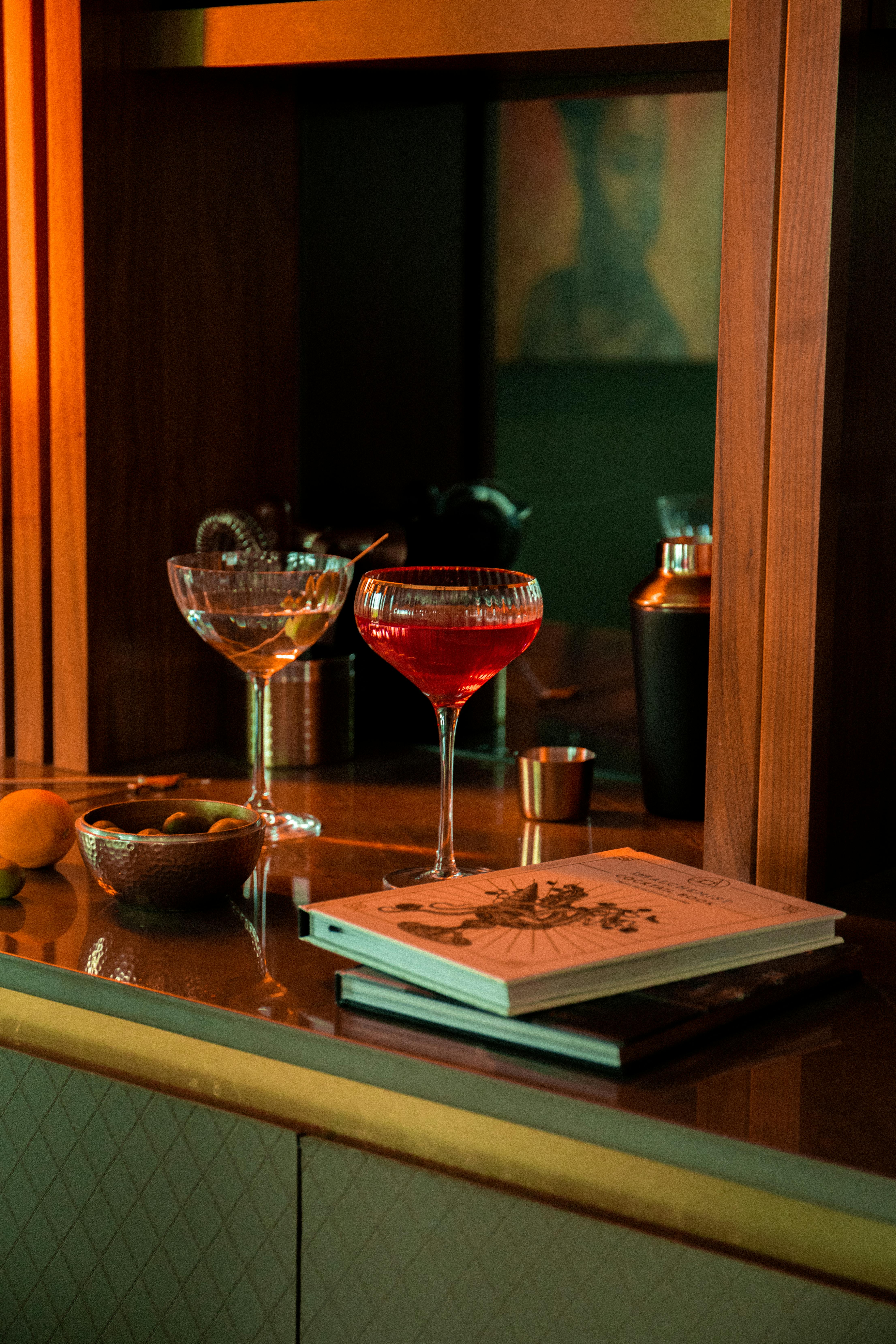 A stylish bar scene with red cocktail, glasses, books, and decor.