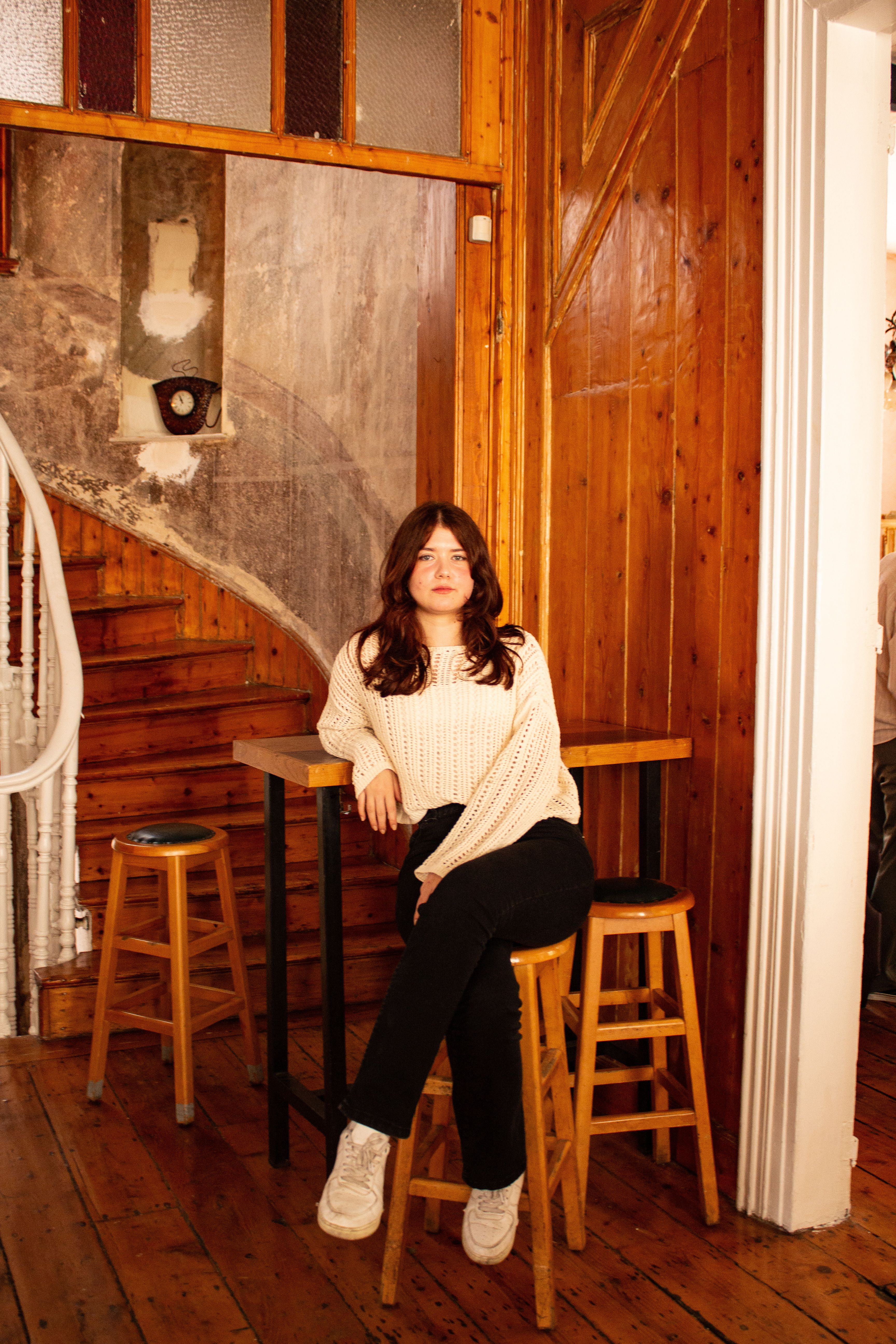 A stylish woman sits confidently in a cozy, rustic room with wooden accents.