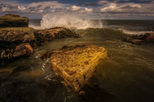 Free A dramatic scene of ocean waves crashing against a rocky shore with stormy skies. Stock Photo