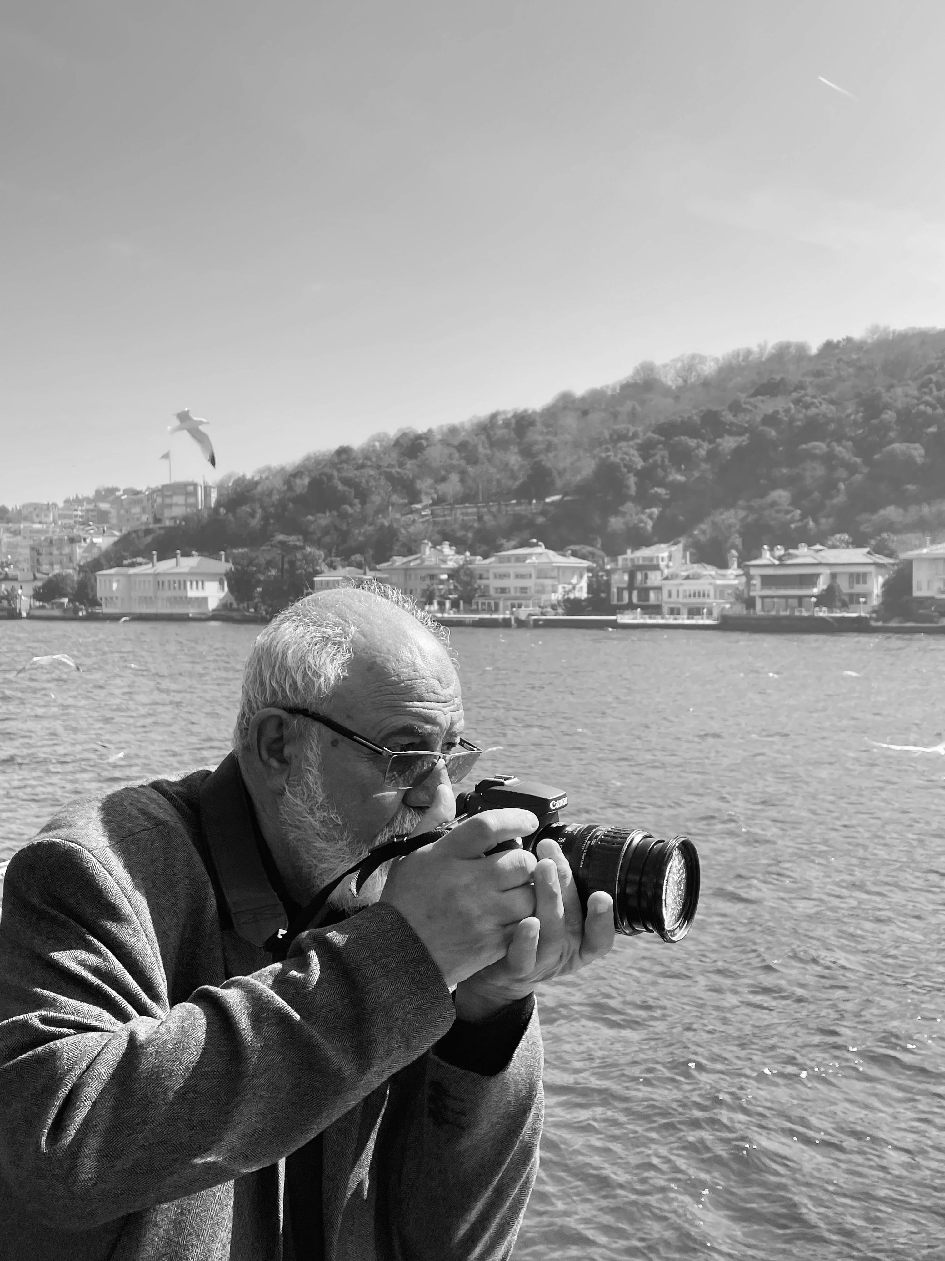 Senior man photographs the Bosphorus waterfront in İstanbul, Türkiye.