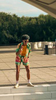 A fashionable young adult on a skateboard in a bright, summer outfit.