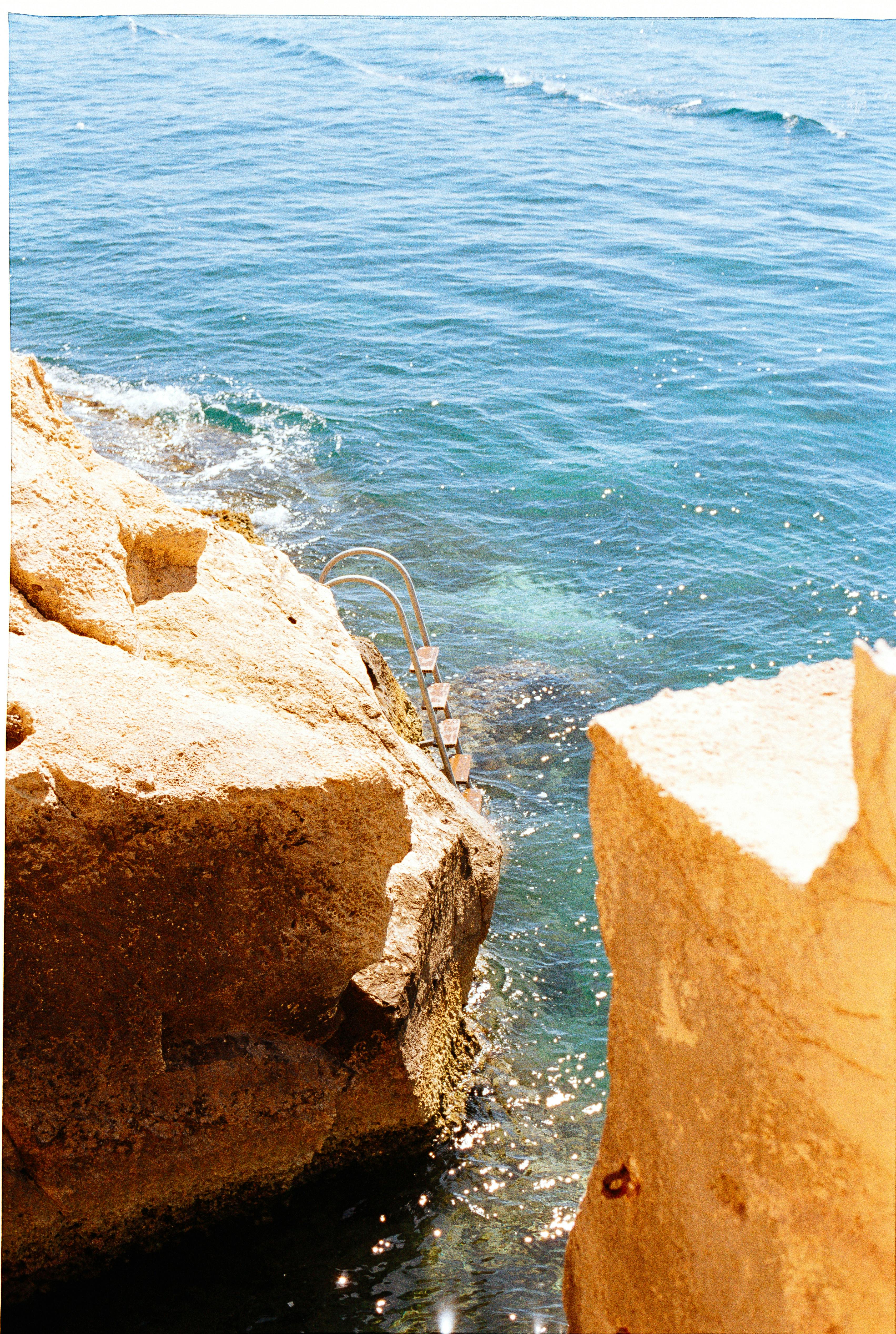 Serene ocean scene with sunlit rocky cliffs and turquoise waters, perfect for a summer getaway.