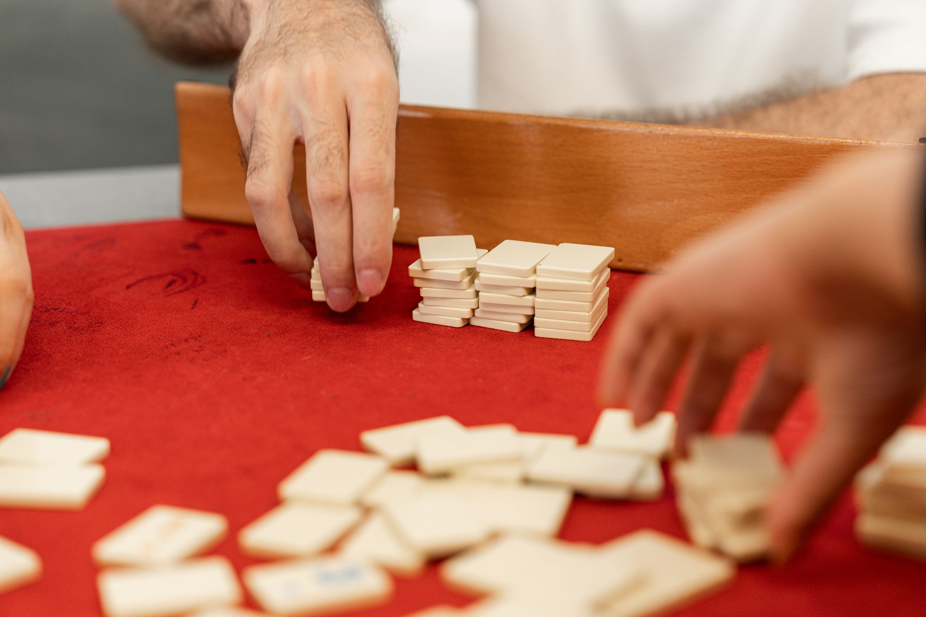 Hands engaging in a traditional board game with tiles on a red felt table.