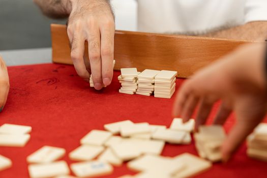 Hands engaging in a traditional board game with tiles on a red felt table.