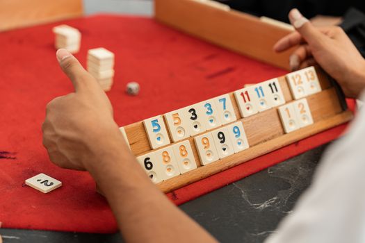 Hands of players arranging tiles during a Rummikub game on a red table, capturing strategic gameplay moments.