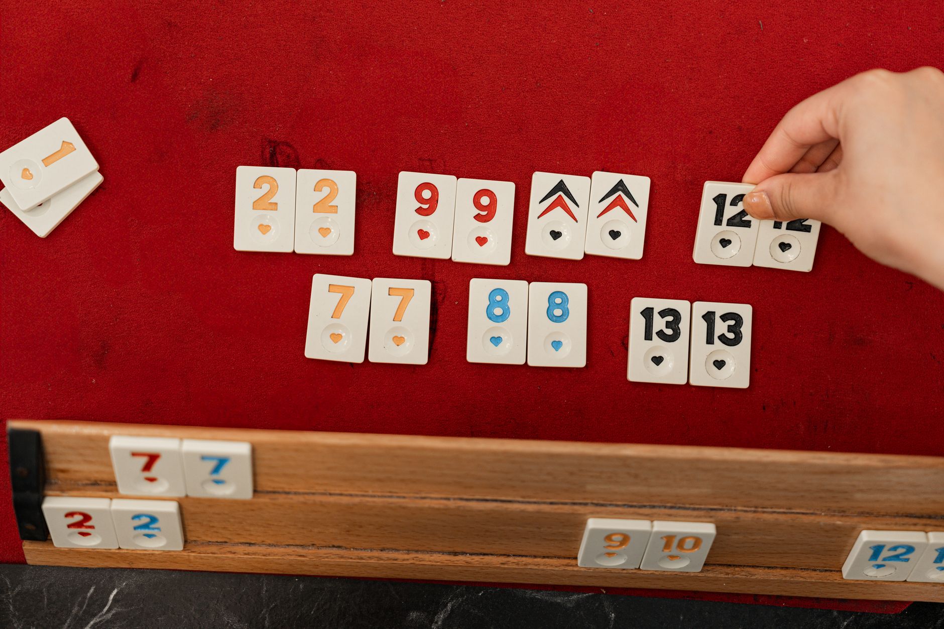 A hand arranging rummy tiles on a red felt table, ideal for leisure themes.