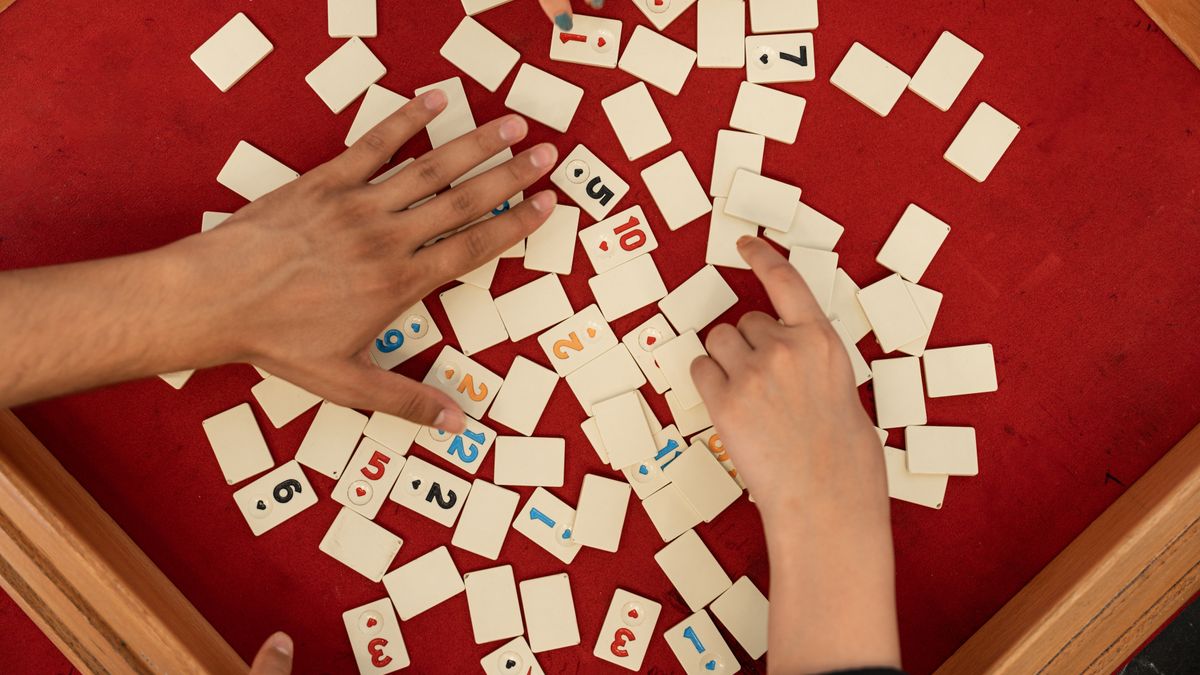 Tre händer flyttar spelbrickor på ett rött spelbord