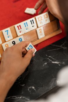 Close-up of a person arranging numbered tiles on a Rummikub board indoors, focusing on hands and tile numbers.