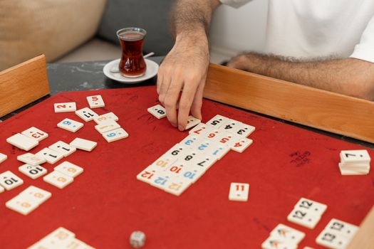 Man playing Rummikub in a cozy indoor setting with tea.