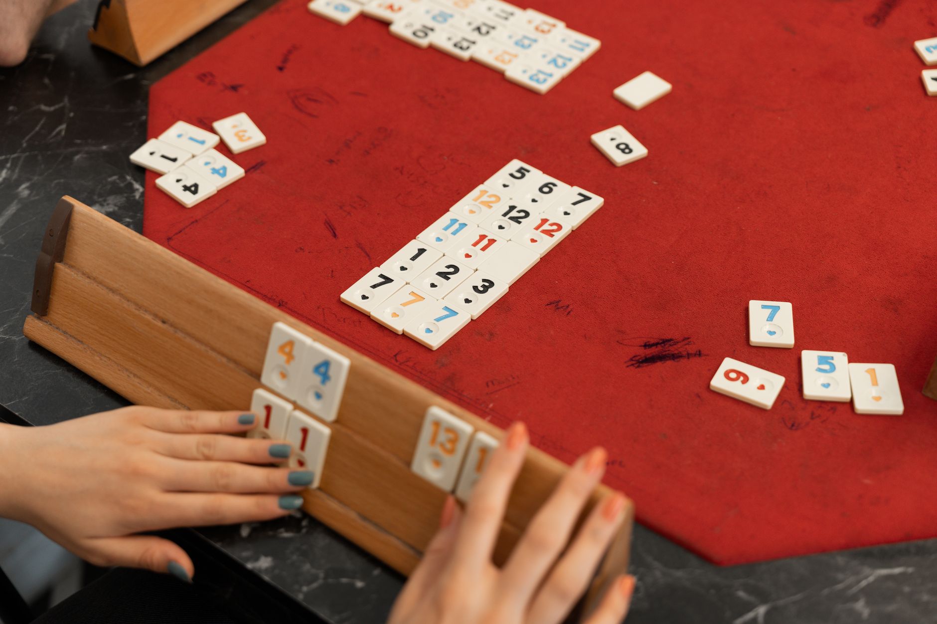 Close-up of players enjoying a game of Okey indoors on a red felt table, emphasizing numbers and strategy.