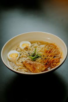 A steaming bowl of ramen with soft-boiled eggs, grilled chicken, and vegetables, perfect for a cozy meal.