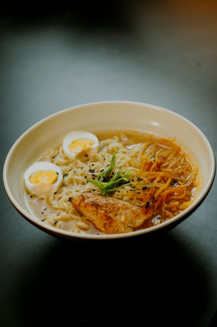 A steaming bowl of ramen with soft-boiled eggs, grilled chicken, and vegetables, perfect for a cozy meal.