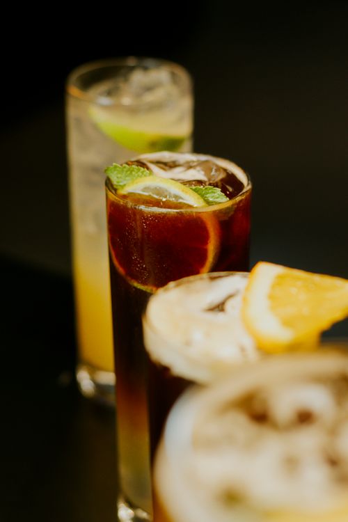 Free Three vibrant cocktails with citrus garnishes featuring lemon, lime, and mint, captured indoors on a dark background. Stock Photo