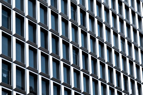 Free Close-up of a modern building facade with repetitive glass window pattern. Stock Photo