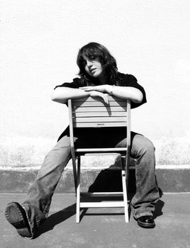 Artistic black and white portrait of a woman casually seated on a chair outdoors, embodying a relaxed and contemplative mood.