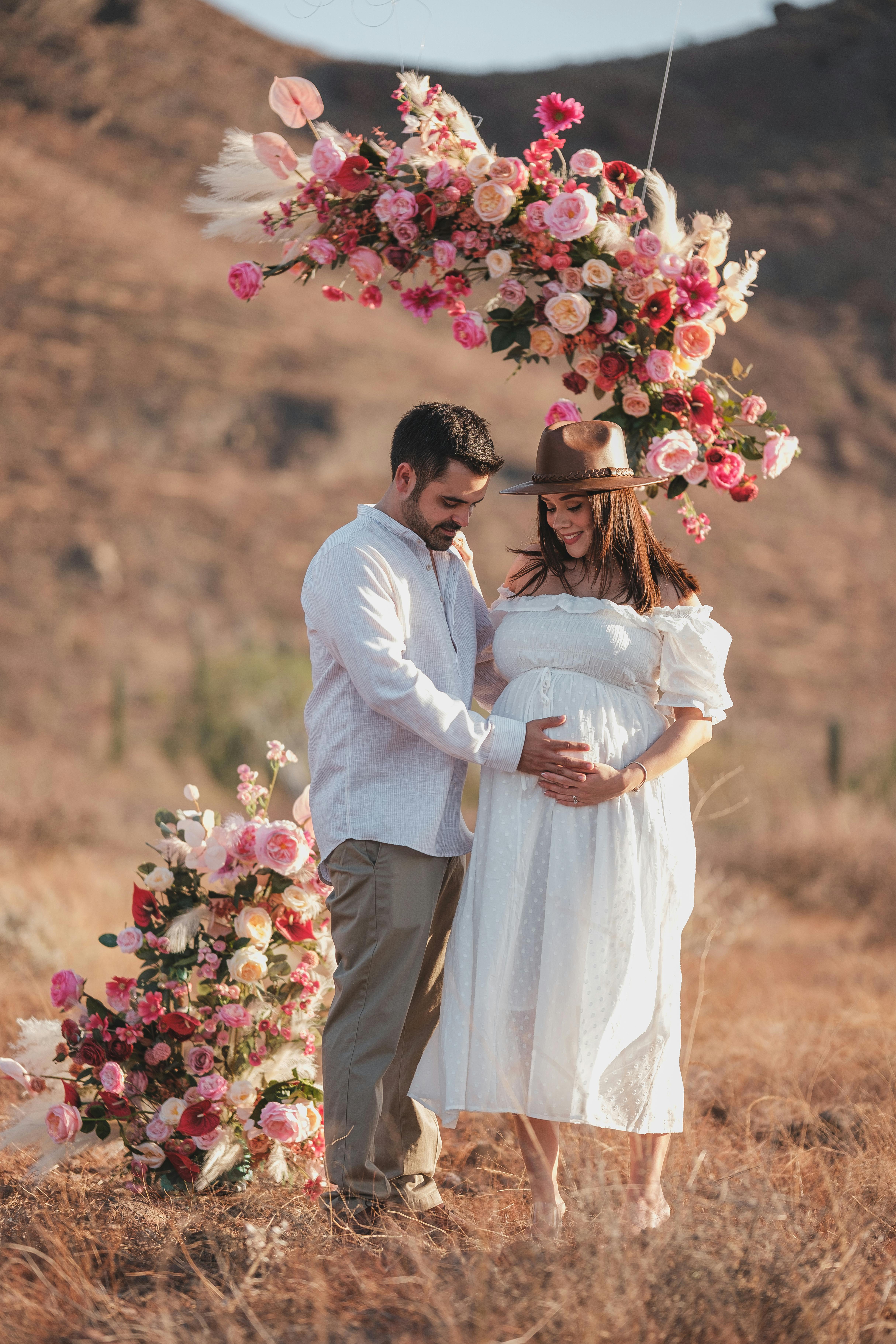 a pregnant couple standing under a floral arch in the desert