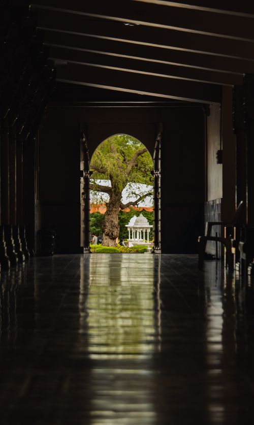 Free Dark hallway opens to a bright garden view framed by an archway, creating a mysterious and inviting scene. Stock Photo