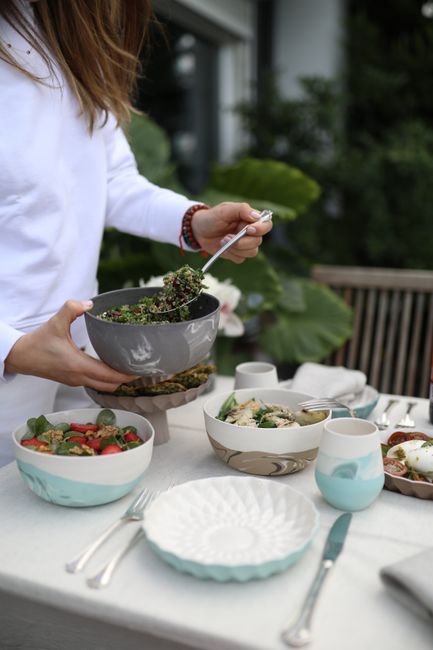 Person serving fresh salads at an outdoor dining table with stylish tableware.