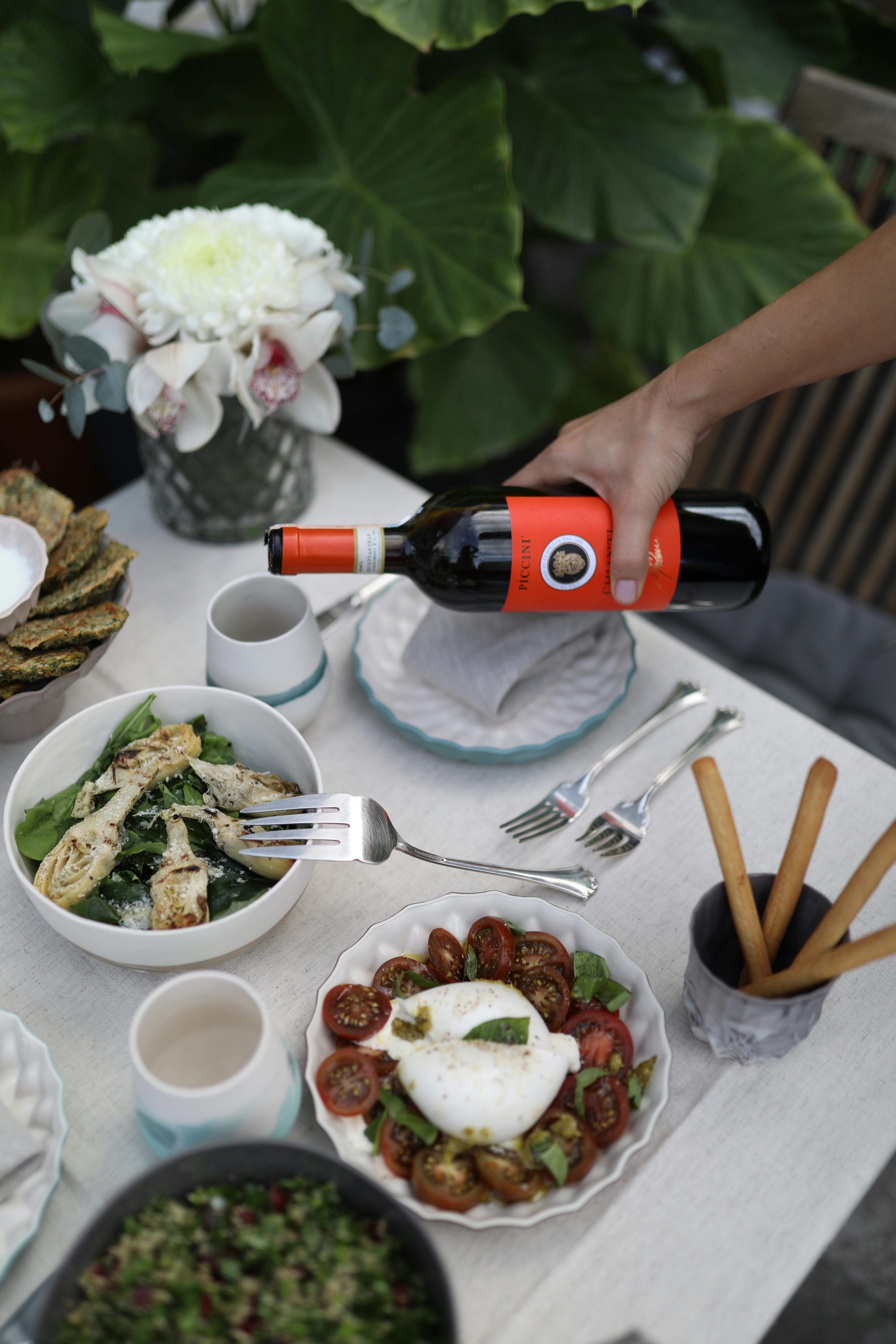 A serene outdoor meal featuring wine, salad, and fresh flowers, perfect for a garden dinner setting.