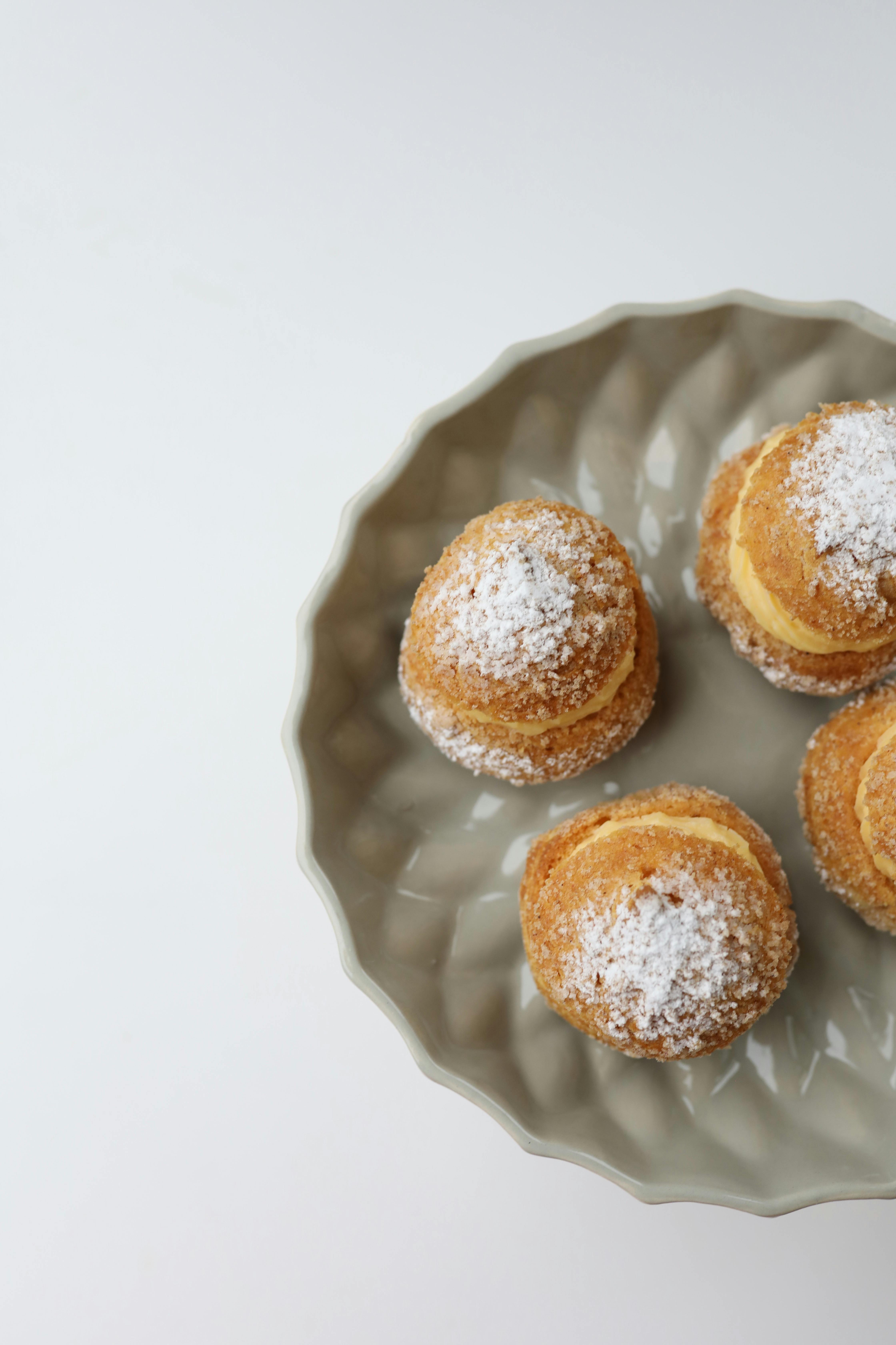 Delicious cream puffs with powdered sugar on a decorative plate.