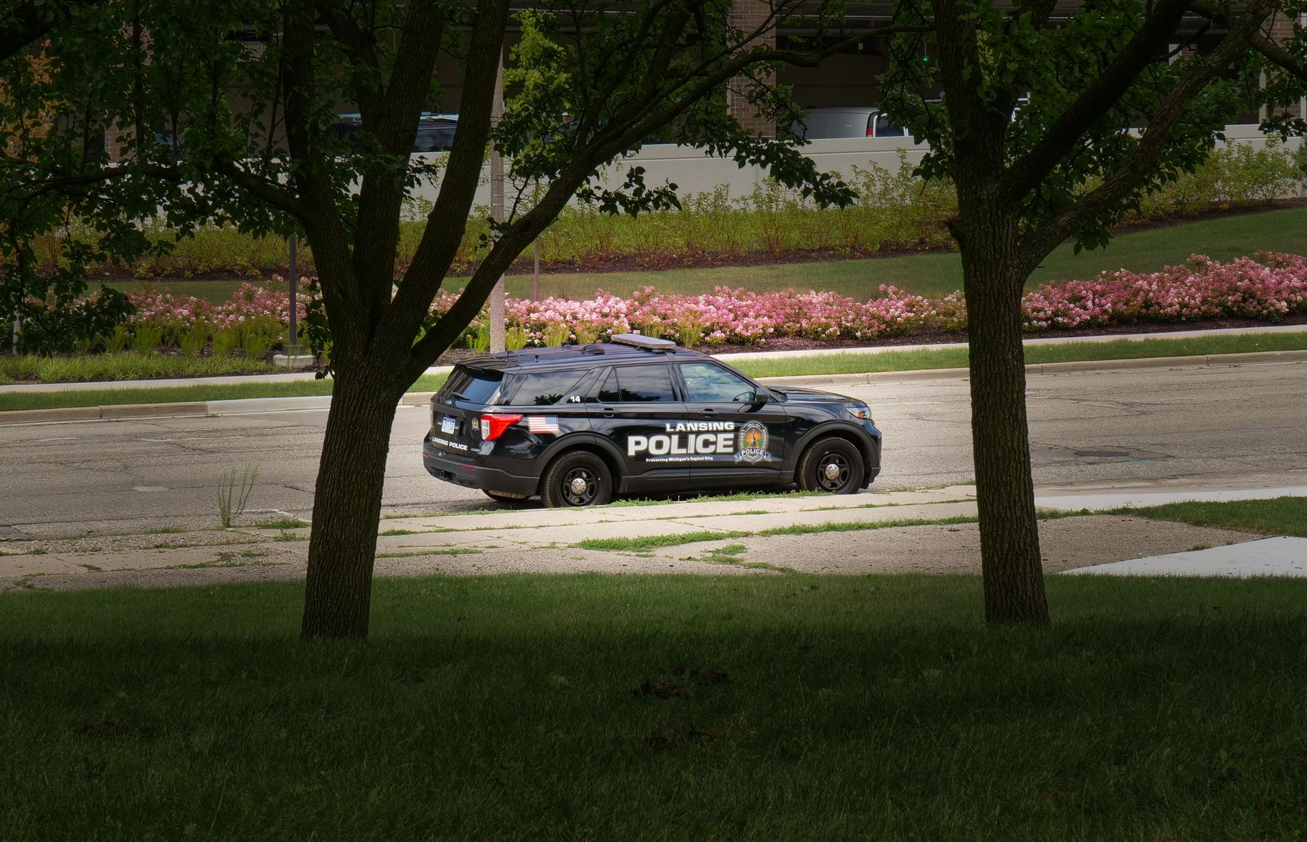 Lansing police vehicle parked in a lush city park with flowers and trees.