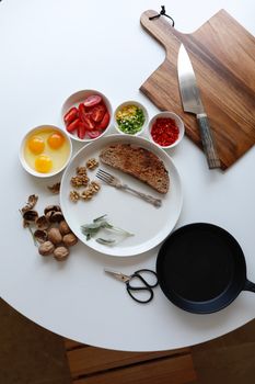 Top view of fresh breakfast ingredients, including eggs and vegetables, on a rustic table setting.