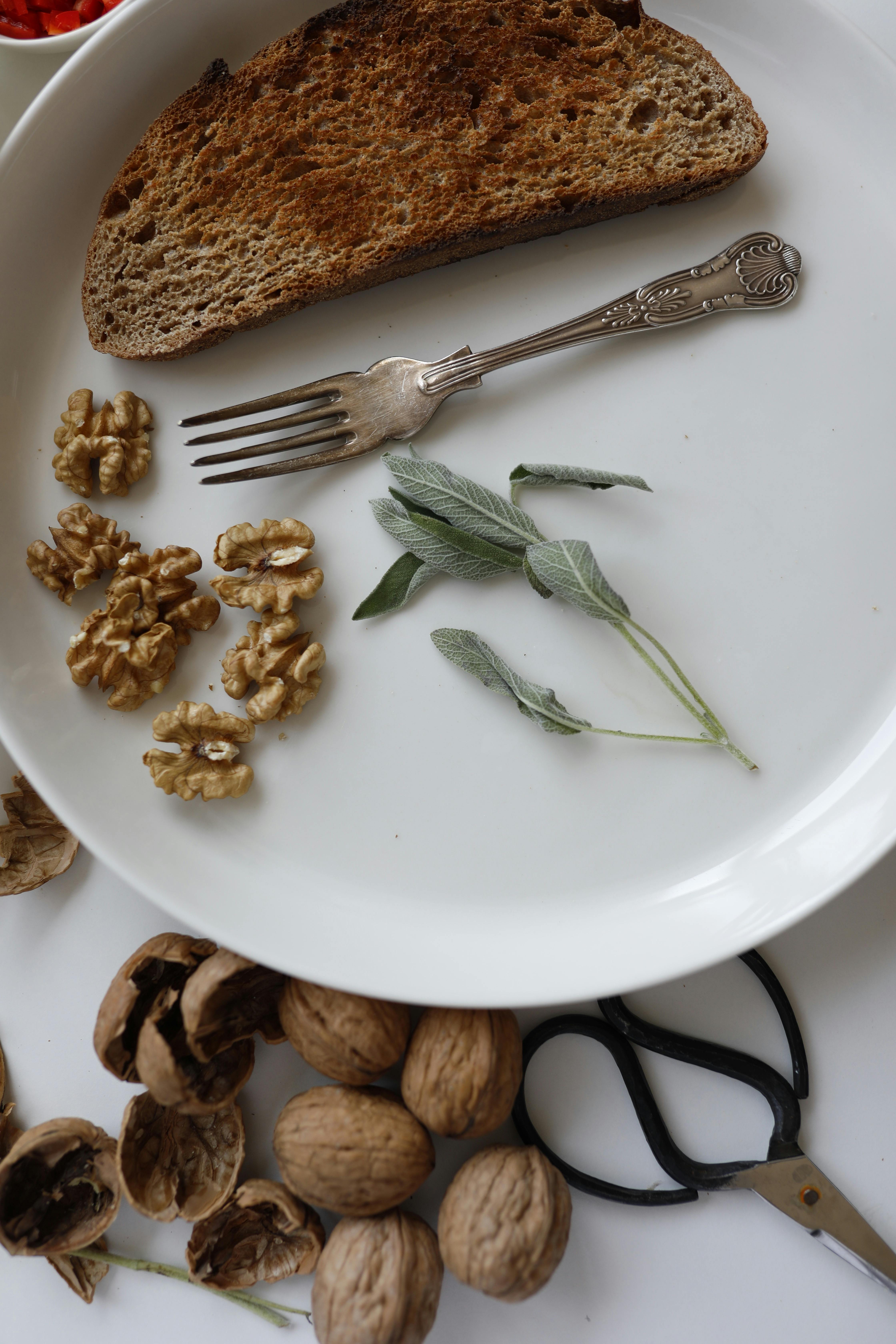 A still life image of toast, walnuts, and herbs on a plate with vintage fork.