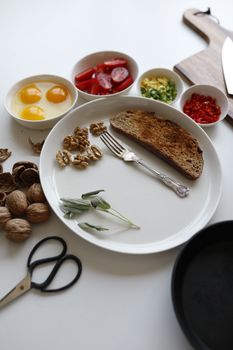 Flat lay of breakfast ingredients with bread, eggs, and vegetables on a white plate.