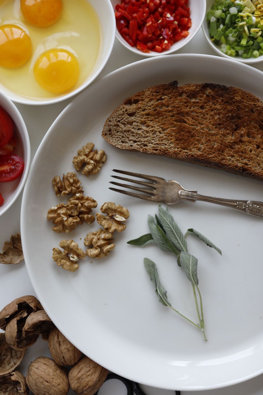Flat lay of ingredients for a nutritious breakfast including walnuts, eggs, and toast with herbs.
