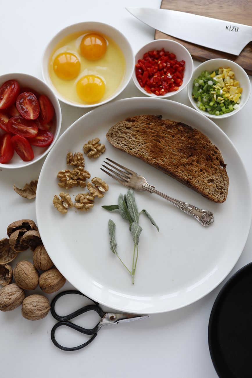 A selection of fresh breakfast ingredients arranged on a flat lay, including rustic bread and eggs.