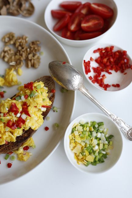 Delicious breakfast toast topped with scrambled eggs, peppers, and fresh ingredients, served with walnuts and tomatoes.