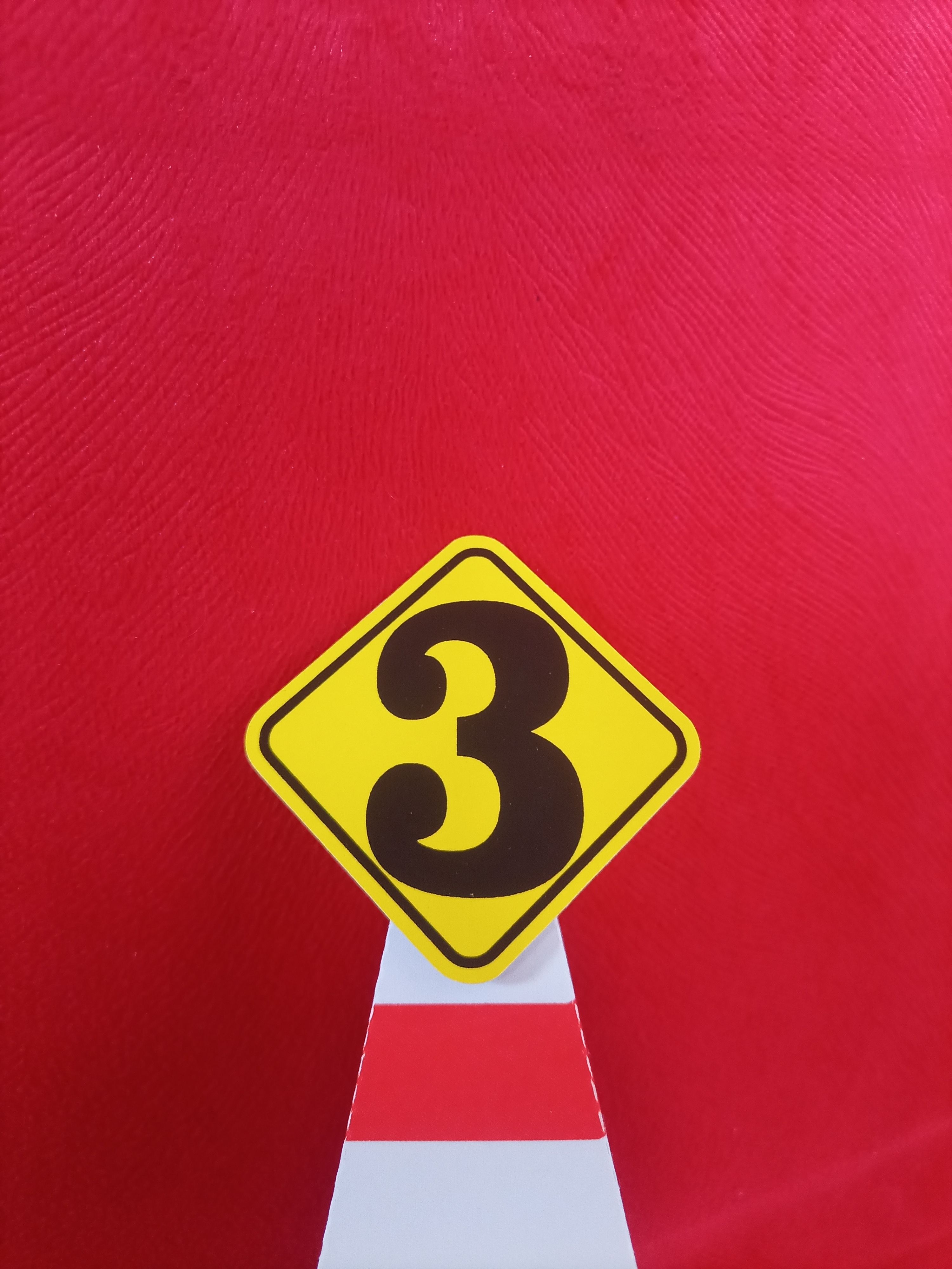 Yellow number 3 sign on a red textured background symbolizing caution or warning.