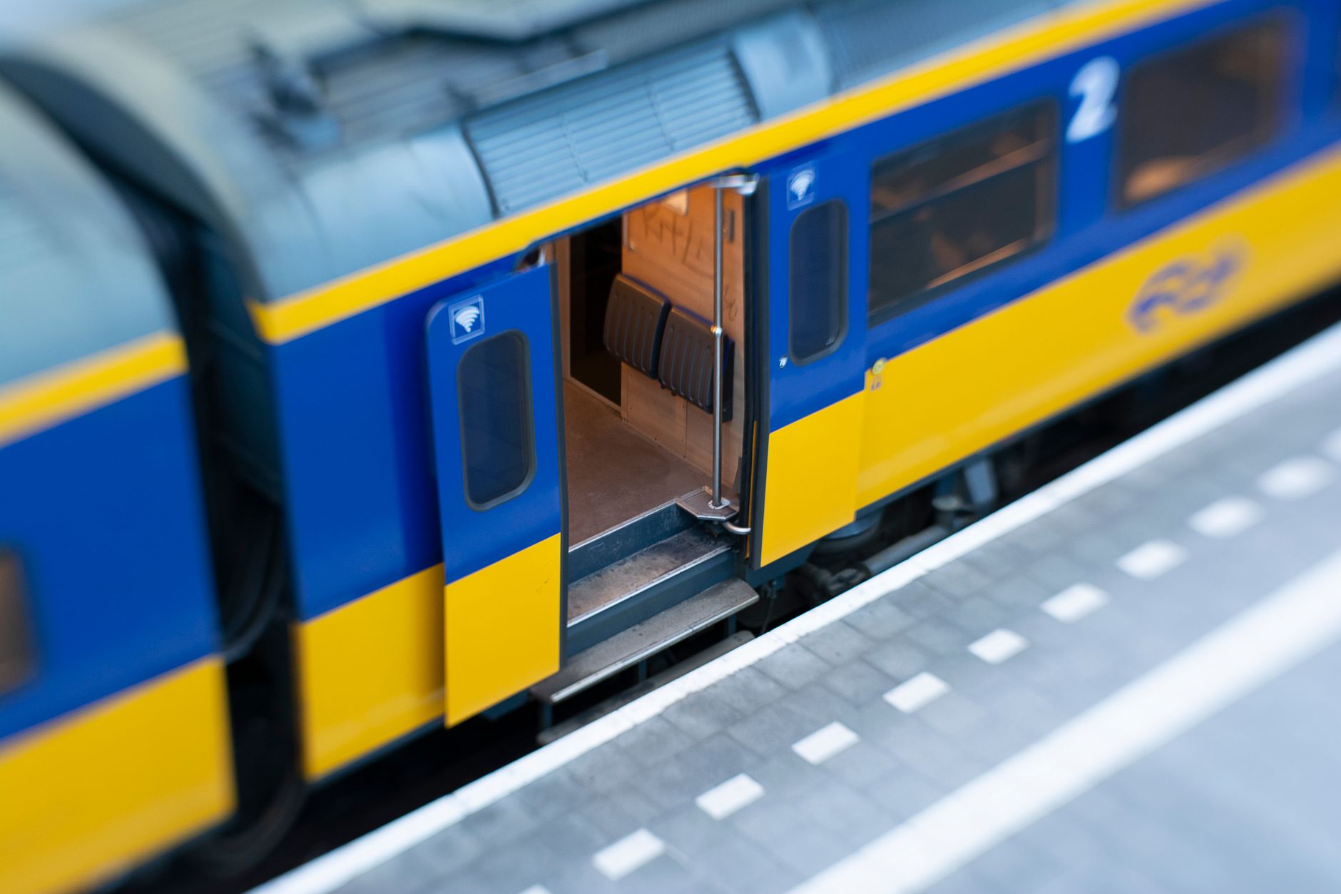 A blue and yellow train with an open door at an empty station, highlighting modern rail travel.