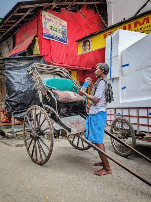 Free A man stands with a traditional hand-pulled rickshaw on a busy street in Kolkata, India. Stock Photo