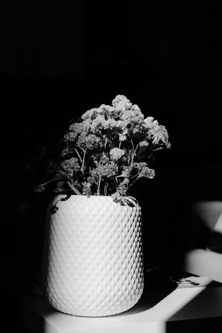 Black and white photo of a flower arrangement in a textured vase with dramatic lighting.