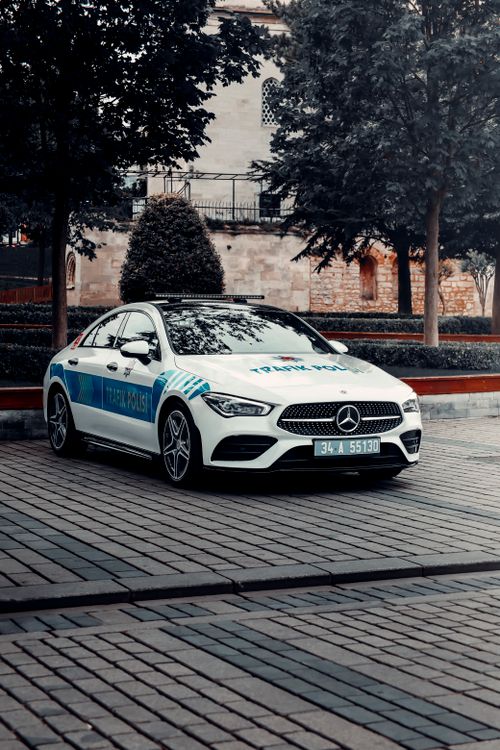 Free A sleek white Mercedes traffic police car parked on a cobblestone city street surrounded by trees. Stock Photo