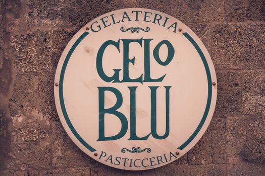 Rustic sign reading 'Gelateria Gelo Blu' on a textured brick wall. Perfect for urban and vintage themes.
