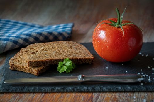 A rustic still life featuring fresh tomato and whole grain bread on a slate board.