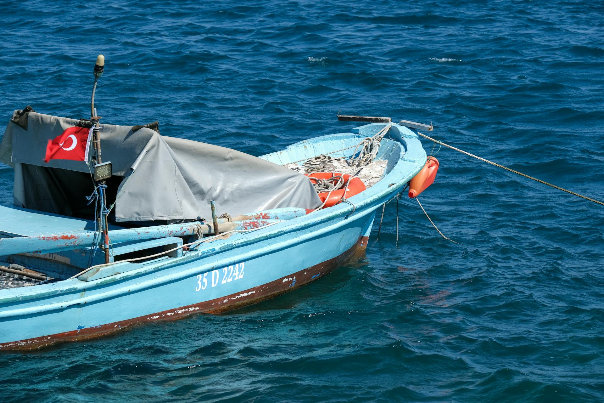 A small traditional fishing boat with a Turkish flag moored in calm blue waters, showcasing maritime leisure.