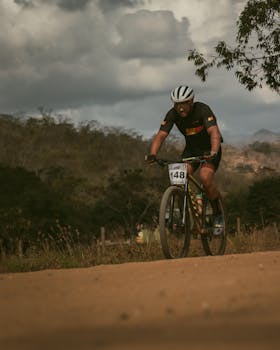 An adult male cyclist racing on a dirt trail wearing a helmet and sports gear.