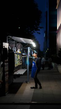 Person standing at a food truck on a dimly lit city street at night.