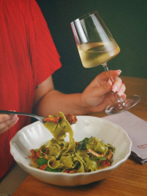 Free Close-up of a woman enjoying green pasta with vegetables and white wine. Stock Photo