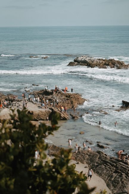 A lively day at Laguna Beach with people enjoying the sun and surf on the rocky shore.