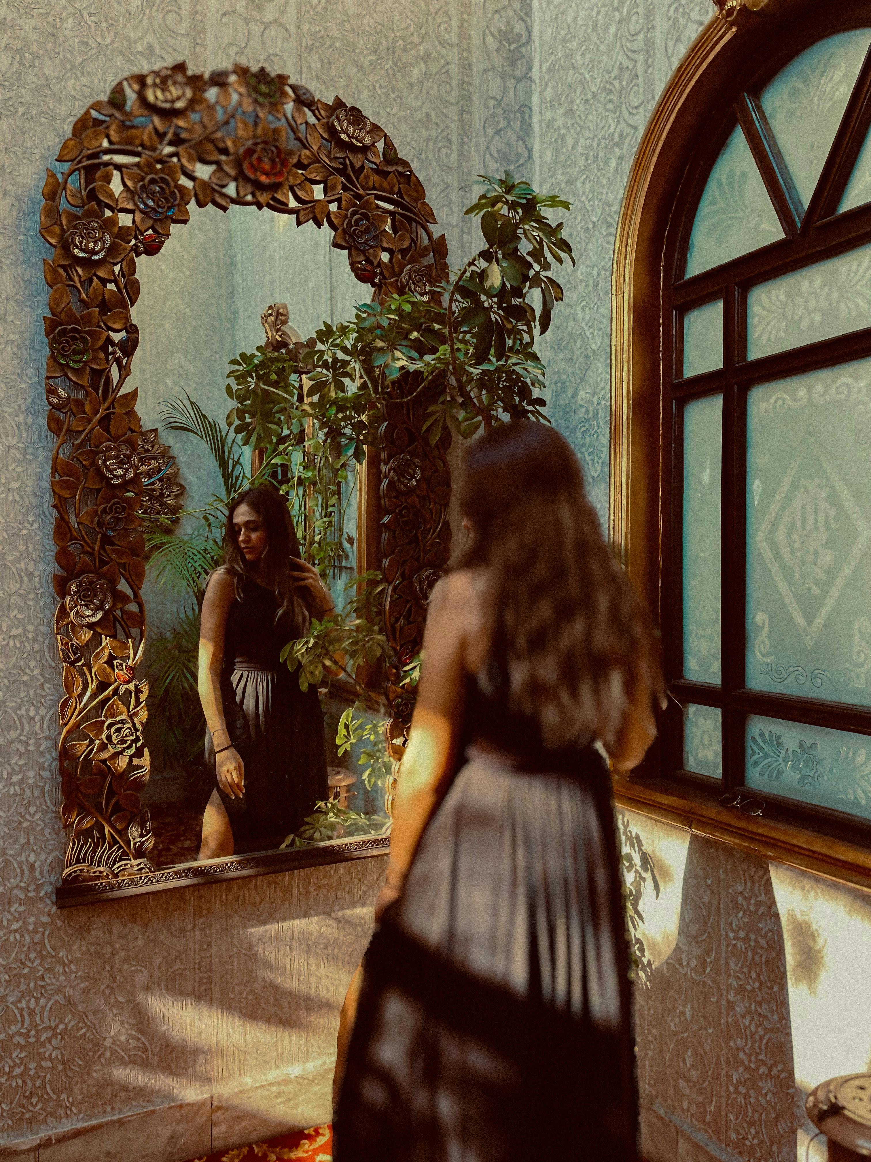 a woman in a black dress looking at a mirror