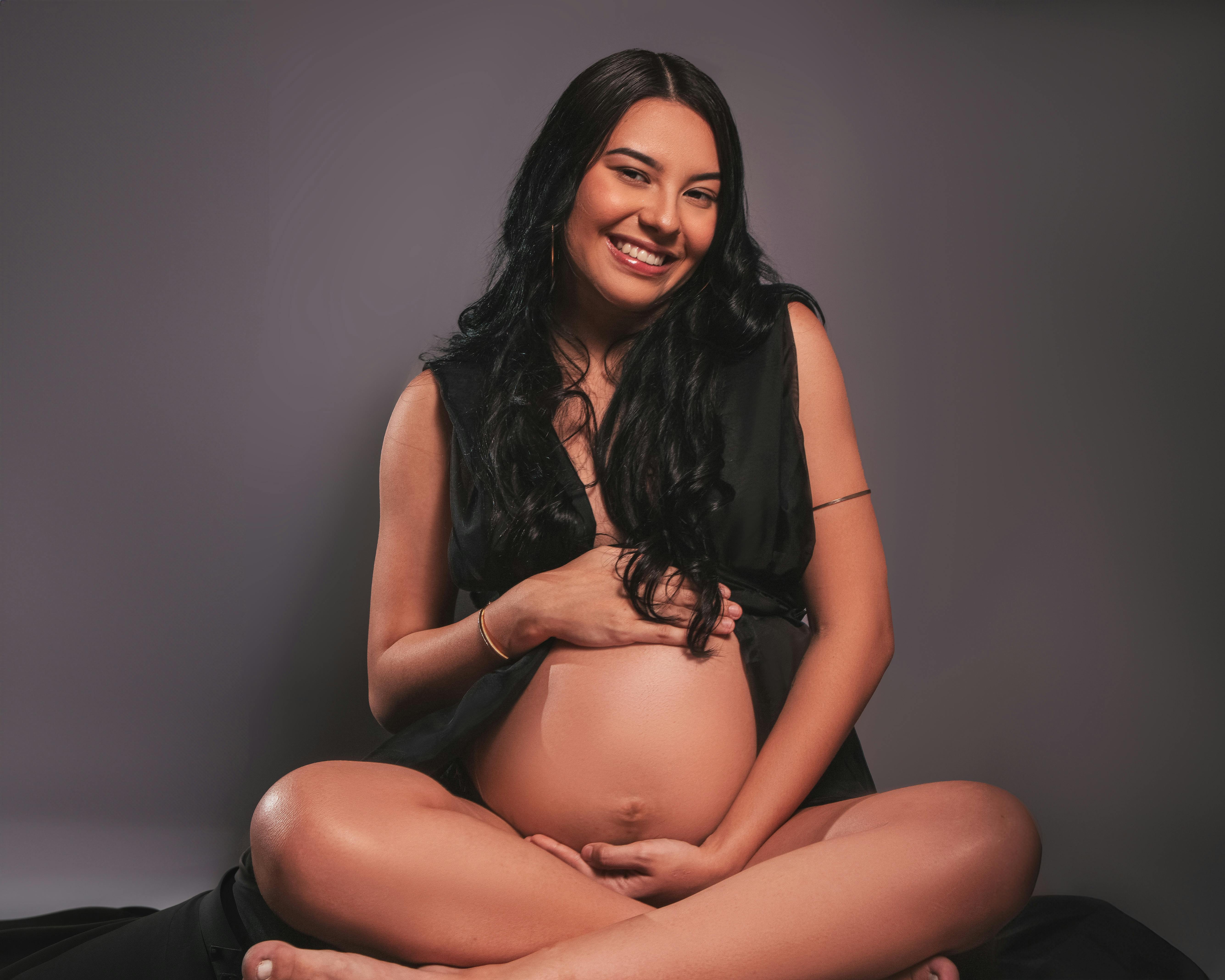 a pregnant woman in black sitting on a gray background