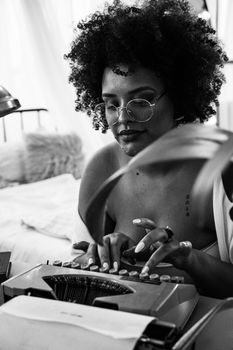 Black and white portrait of a woman typing on a vintage typewriter, showcasing creativity and style.