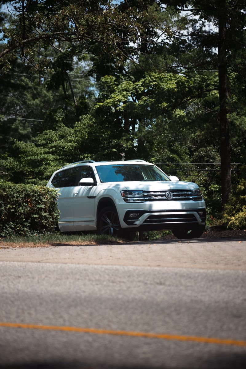A white SUV parked alongside a forested road in daylight