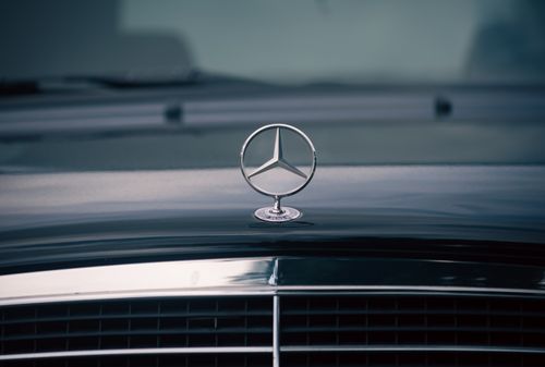 Free Close-up of a shiny luxury car hood emblem reflecting light on the road. Stock Photo