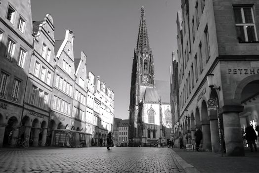 Black and white photo of a gothic cathedral in a European city square, showcasing classic architecture.